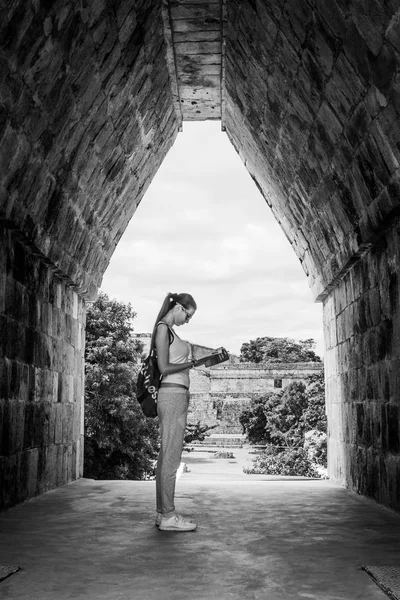 Black and white picture of a woman reading a book under an arch at the Uxmal archaeological site, Yucatan, Mexico.