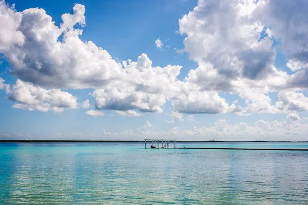 Beyaz bulutlar ve Laguna Bacalar, Chetumal, Quintana Roo, Meksika mavi lagün su ile Pier.