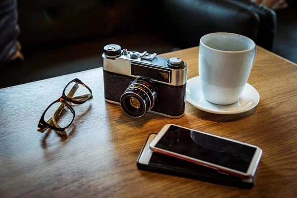 Vintage camera with coffee cup, glasses and smartphone on the ta — Stock Photo, Image