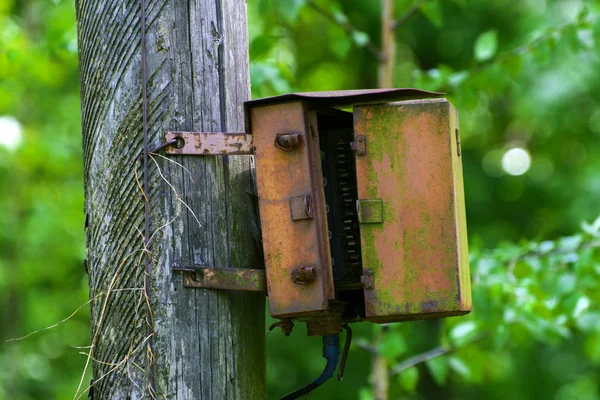 Uma velha caixa de junção elétrica enferrujada em um poste de madeira — Fotografia de Stock