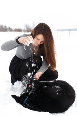 Genç esmer kız karlı bahçede köpeğiyle oynuyor..