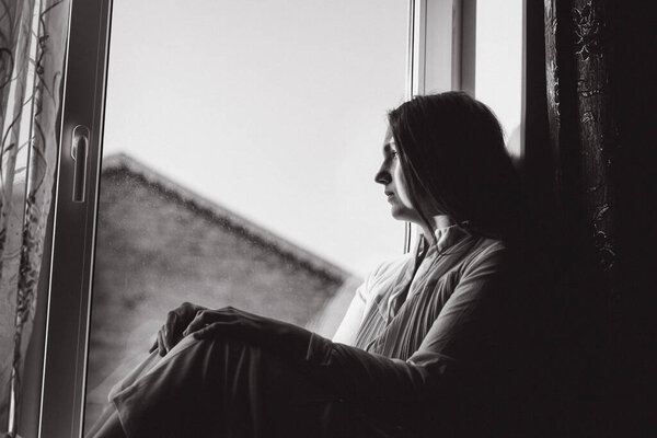 Black and white photography of girl sitting on the window.