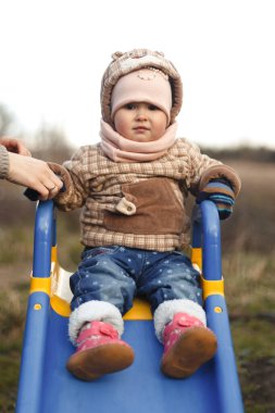 Mutlu bir çocuk bir çocuk kaydırağında oturur ve şık bir şekilde gülümser.