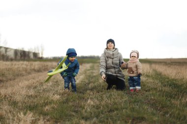 İki çocuklu genç bir anne, küçük bir kız ve sonbahar tarlasında oynayan bir oğlan. Parktaki sonbahar ailesi oyuncak uçakla oynuyor..
