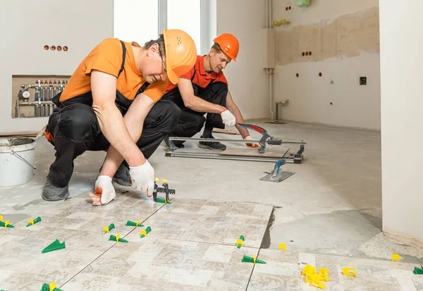 İki işçi yere seramik fayanslar yerleştiriyor..