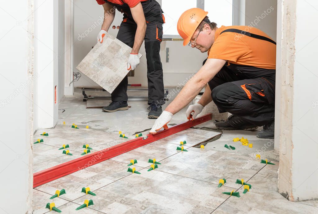 Two workers are installing ceramic tiles on the floor.