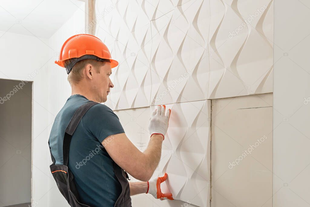 Installation of gypsum 3D panel. The worker is attaching the gypsum tile to the wall.