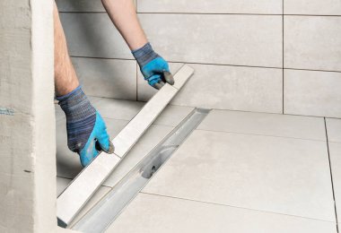 Bir işçi banyoya seramik fayanslarla dekore edilmiş bir drenaj kapağı yerleştiriyor..
