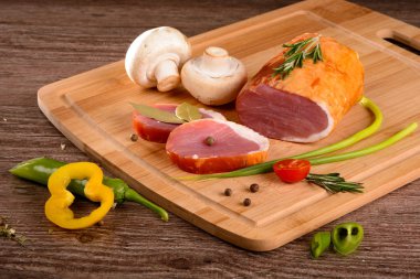 Füme sığır filetosu parça dinlenirken ahşap bir gemide, dilimlenmiş taze sebze yanında yatıyordu