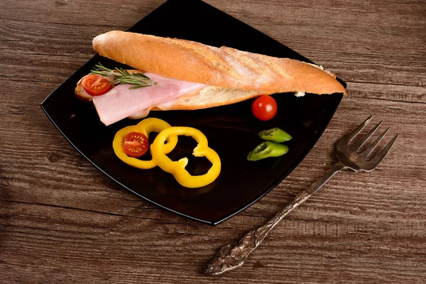 Grande sanduíche com lombo fumado, encontra-se na placa preta ao lado de legumes — Fotografia de Stock