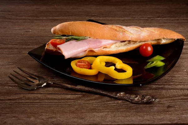 Grande sanduíche com lombo fumado, encontra-se na placa preta ao lado de legumes — Fotografia de Stock