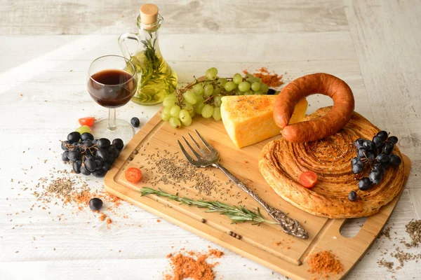 Колбаса, сыр, хлеб, виноград, бокал красного вина на деревянной доске — стоковое фото