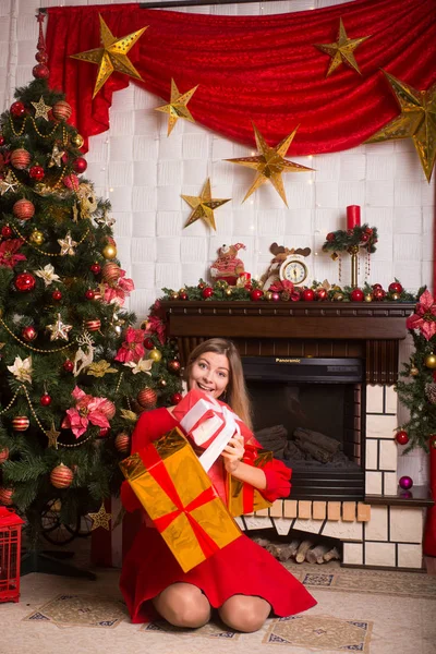 Красива дівчина з подарунками в червоній сукні біля ялинки зима Новий рік — стокове фото