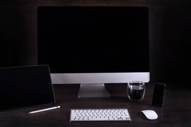 kahverengi Masa ve bir filme kamera, kahve bardağı, telefon, tablet Pc, karanlık bir duvara karşı odada siyah bilgisayar ekranı
