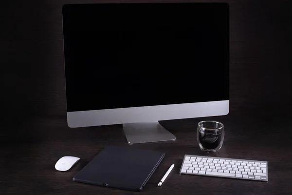 black computer screen in the room on a brown table , coffee mug, phone,tablet PC, against a dark wall