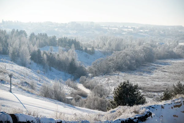 Rural winter landscape with white frost in a ravine with trees