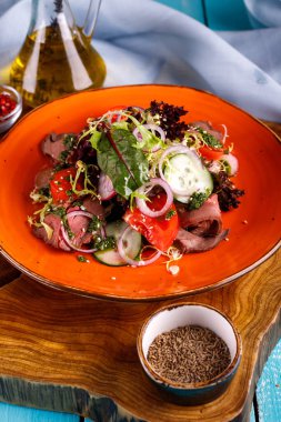 Dilimlenmiş biftekli salata, domates, ahşap arka planda bir tabakta salatalık.