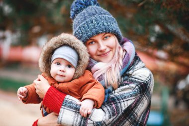 Sonbaharda kollarında küçük bir oğlu olan şık, genç bir anne yürüyor. Yeşil ot ve sarı yapraklar.