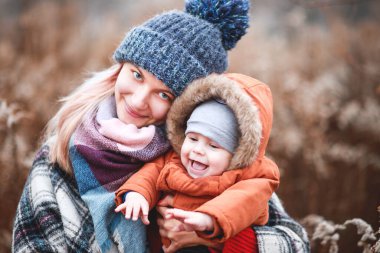 Kollarında küçük bir oğlu olan şık, genç bir anne sonbahar ormanında yürüyor. Yeşil ot ve sarı yapraklar.