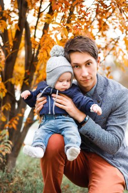 Genç bir oğul, sonbahar geçmişinde genç bir babanın kollarında oturuyor.