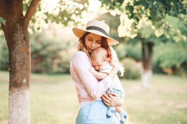 Bir anne çocuğunu doğada güneşin batışının arka planına karşı kucaklıyor.