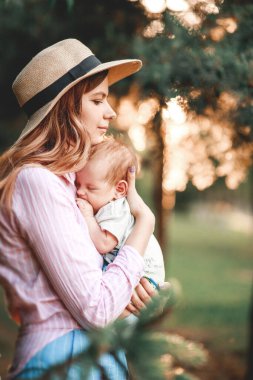 Bir anne çocuğunu doğada güneşin batışının arka planına karşı kucaklıyor.