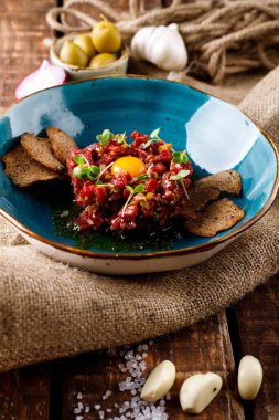 Çuval bezinin arka planında mavi bir tabakta salatalık turşulu sığır eti tartar.