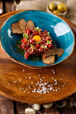 Ahşap arka planda mavi tabakta salatalık turşulu sığır eti tartar.