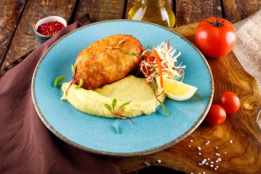 Tahta bir masanın arka planında patates püresi ve sebzeyle servis edilen et pirzolası.