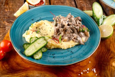 Gulaş, ahşap bir masa ve kumaş üzerinde patates püresi ve sebzelerle servis edilir.