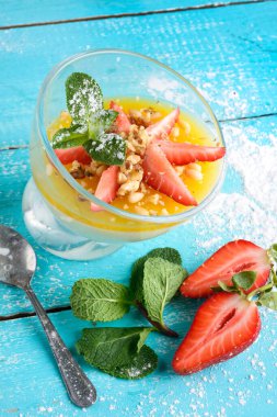 Lezzetli panna cotta mavi arka planda, çilek ve nanenin yanında.