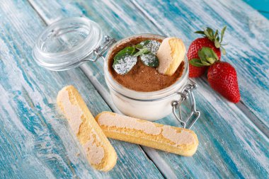 tiramisu cam bir fincanda, tahta bir masada, nane ve simit yanında.
