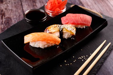 Ahşap bir masanın arka planında siyah bir tabakta çubuklu suşi.