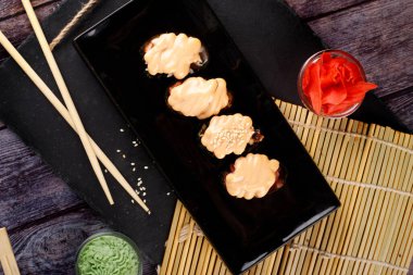 Pişmiş suşi, susam tohumları serpiştirilmiş rulo, siyah bir tabağa yakın çekim.