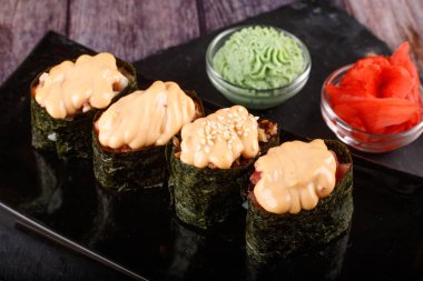 Pişmiş suşi, susam tohumları serpiştirilmiş rulo, siyah bir tabağa yakın çekim.