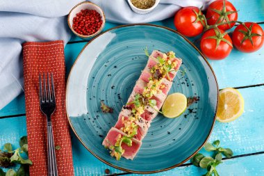 Mavi tabakta susam tohumlu dilimlenmiş ton balığı bifteği ahşap bir masaya karşı.