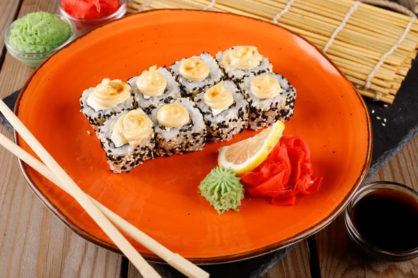 Baked sushi, rolls sprinkled with sesame seeds, close-up on an orange plate