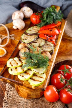 Tahta bir arka planda kesme tahtasında kızarmış sağlıklı sebzeler.