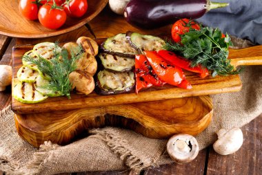 Tahta bir arka planda kesme tahtasında kızarmış sağlıklı sebzeler.