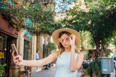 Şık bir kız, bir yaz günü Barselona caddesinde akıllı telefonuyla selfie çekerken gülümser.