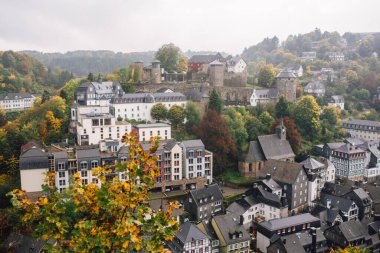 Eski şehrin bulutlu sonbahar manzarası. Monschau, Almanya. Yeşil tepeler ve gri mika çatılar.