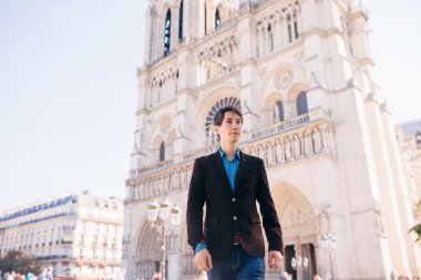 Genç bir adam Paris 'teki Notre Dame Katedrali' nin arka planına karşı poz veriyor.