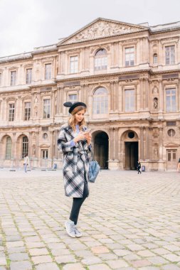 Louvre Müzesi 'nin yanında güzel montlu bir kız duruyor. Fransa ve tarihi binaları ziyaret etme kavramı.