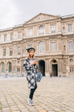 Louvre Müzesi 'nin yanında güzel montlu bir kız duruyor. Fransa ve tarihi binaları ziyaret etme kavramı.