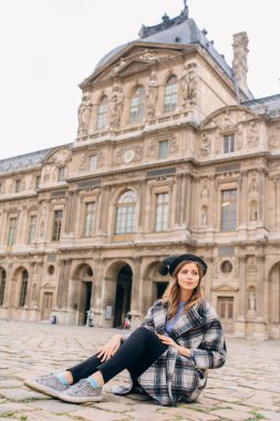 Louvre Müzesi 'nin yanında güzel montlu bir kız duruyor. Fransa ve tarihi binaları ziyaret etme kavramı.