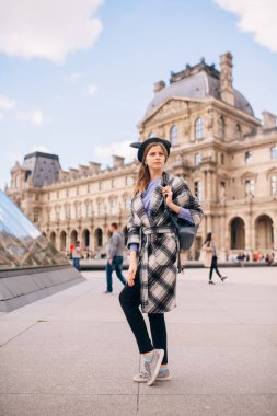 Louvre Müzesi 'nin yanında güzel montlu bir kız duruyor. Fransa ve tarihi binaları ziyaret etme kavramı.