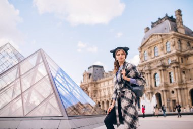 Louvre Müzesi 'nin yanında güzel montlu bir kız duruyor. Fransa ve tarihi binaları ziyaret etme kavramı.