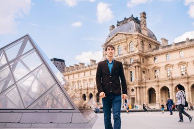 Genç bir adam Louvre binasının arka planında yürüyor. Paris, Fransa