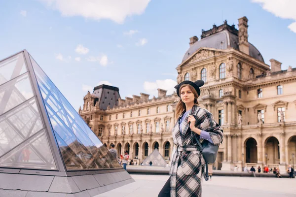 ルーブル美術館の近くに美しいコートを着た女の子が立っています フランスと歴史的建造物の訪問の概念 — ストック写真
