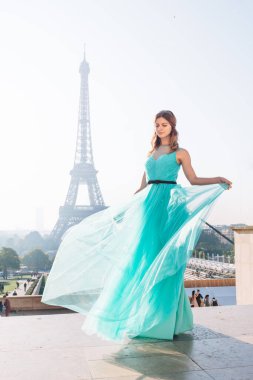 Paris 'teki Eyfel Kulesi' nin arka planında mavi ve yeşil elbiseli güzel ve zarif bir kız duruyor.